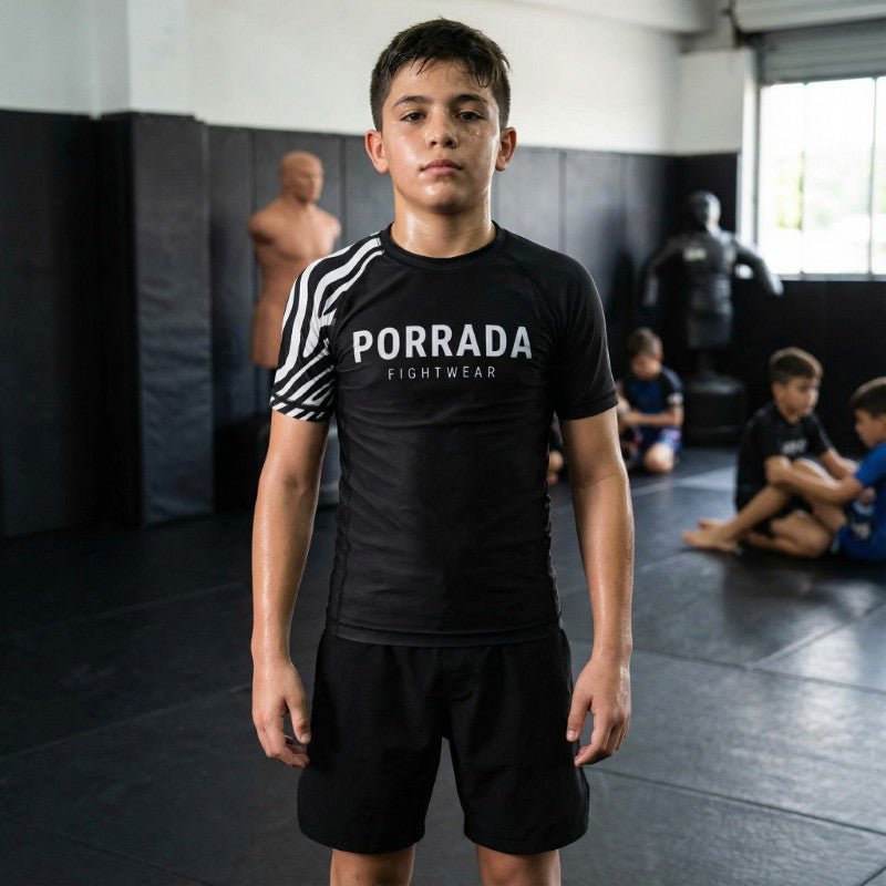 Young athlete wearing Porrada Fightwear kids BJJ rash guard and shorts while training in a martial arts gym.